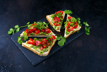 Traditionelles Toast Dreieck Sandwich mit Tomaten, Avocado Aufstrich und Kräuter serviert als Nahaufnahme auf einem schwarzen Design Tablett  - obrazy, fototapety, plakaty