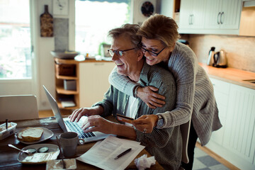 Mature middle aged senior couple online shopping from laptop at home
