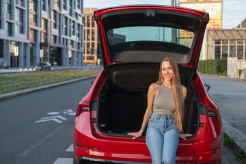 Young blonde woman sitting in the trunk of new red car. 