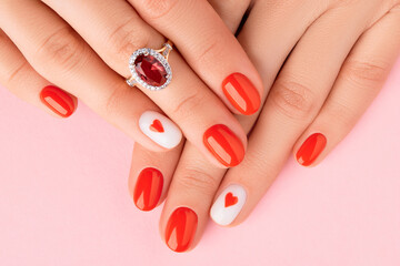 Womans hands with fashionable red manicure on pink background. Manicure, pedicure beauty salon...