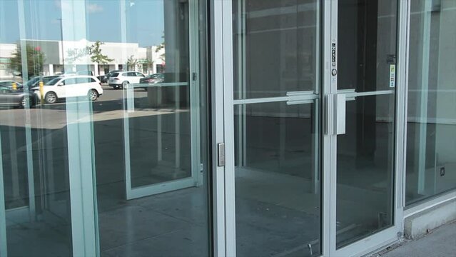 generic glass store doors and windows front entrance with reflection of parking lot and sky and cars vehicles passing