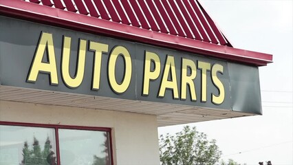 auto parts sign facade with roof above and windows below on storefront with parking lot, yellow writing caption text on black background and red roof, close up
