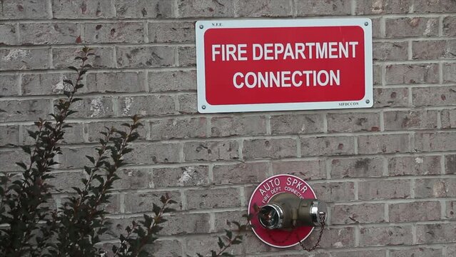 fire department connection sign on beige brick wall with two twin connections below from one spout in red circle auto spkr, white on red