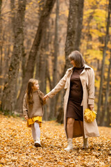 Naklejka na ściany i meble Happy family on an autumn walk. Mother and daughter walking through the park and enjoying the beautiful autumn nature.