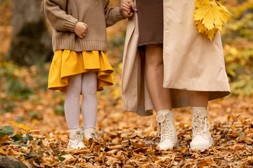 Mom with child little girl walking in autumn park. Closeup of kid and mom legs in shoes walking...