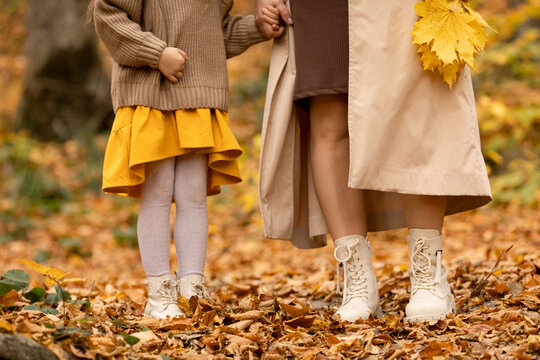 Mom with child little girl walking in autumn park. Closeup of kid and mom legs in shoes walking through fall autumn leaves and foliage
