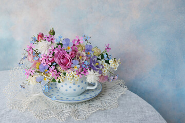 Bouquet of spring and summer flowers in a cup on the table, roses, aquilegia, spirea, forget me not...