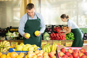 Man seller working in supermarket and lays out fresh apples on counter