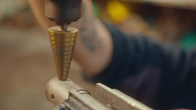 Close-up view of cone shaped drill bit cutting a hole in metal workpiece, hand of unrecognizable worker in the background