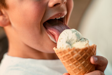 Close-up view of a boy eating ice cream in a waffle cup. Macro. Detailed view of a tongue in ice cream, Summer time, happy childhood. High quality photo - obrazy, fototapety, plakaty