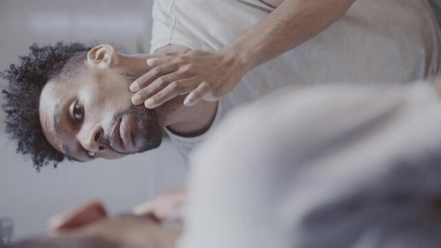 Homem jovem de cabelo jovem conferindo sua barba no espelho do banheiro. Cinematico 4k. Video vertical.