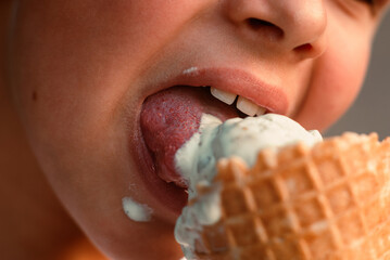 Close-up view of a boy eating ice cream in a waffle cup. Macro. Detailed view of a tongue in ice...