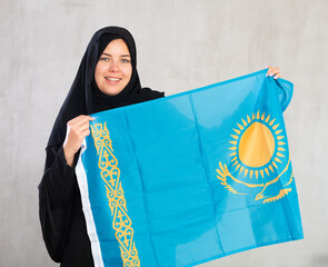 Smiling joyful Muslim woman in traditional black hijab holds flag of Kazakhstan. Portrait of female...