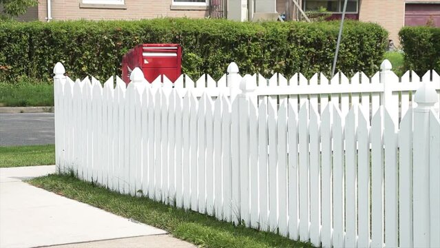 pristine white picket fence with red mailbox and road bush behind