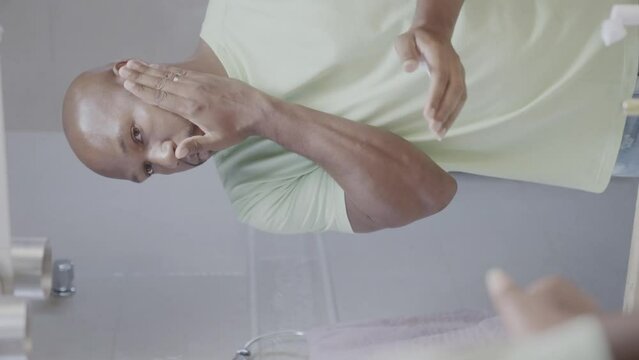 Black man applying shaving foam on his face in front of the mirror. Cinematic 4k. Vertical video.