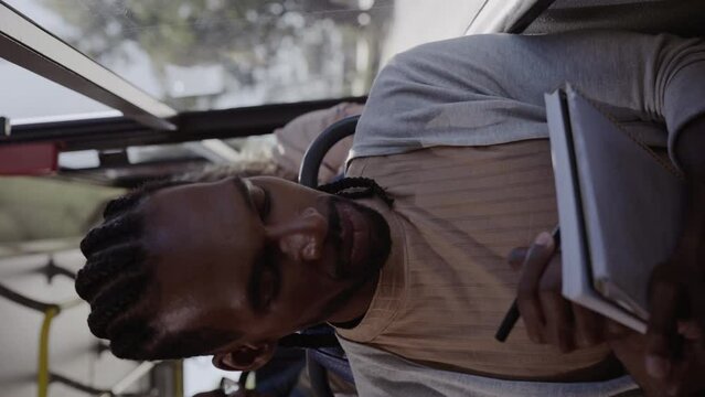 Homem negro jovem escrevendo em um caderno durante trajeto de onibus. Cinematico 4k. Video vertical.