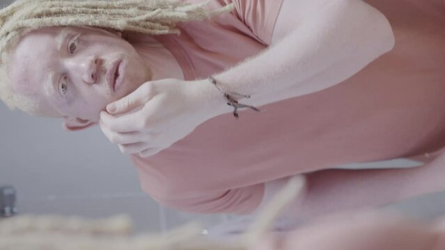 Homem albino com penteado afro aplicando protetor solar no rosto. Reflexo no espelho. Cinematico 4k. Video vertical.