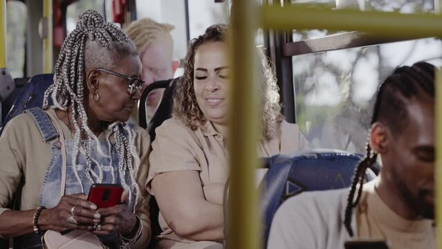Cheerful woman sitting next to lady talking and using smartphone on the bus.Cinematic 4k.