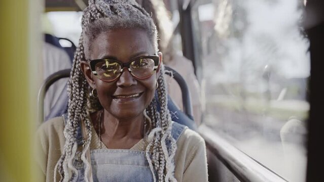 Senior woman with afro hairstyle smiling, sitting in crowded bus. Cinematic 4k.