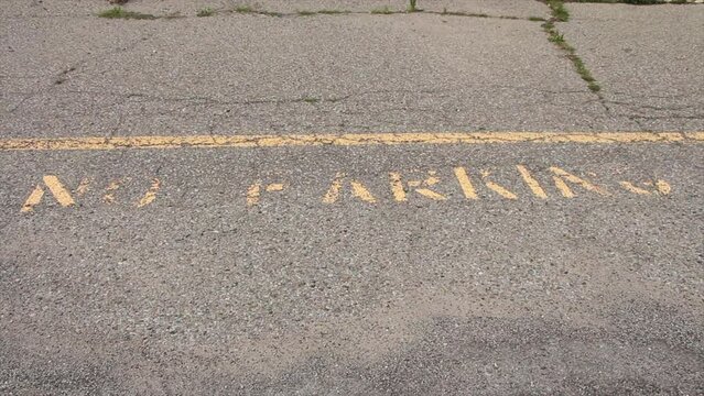 no parking caption print text writing in yellow below line on pavement, worn and faded, shot straight on looking down top of frame