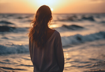 Fototapeta premium Girl standing looking out into the distance. With the sunset and ocean in the background.