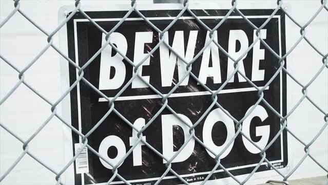 beware of dog black and white rectangle sign against diamond link silver fence with white background behind it