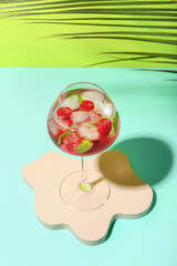 Decorative podium with glass of fresh raspberry mojito and palm leaf on colorful background