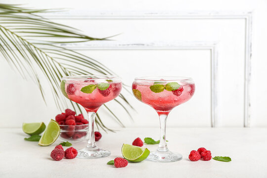 Glasses of fresh raspberry mojito and bowl with berries on white background