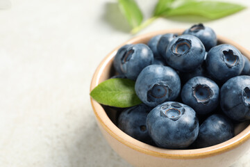 Tasty fresh blueberries in bowl on light grey table, closeup. Space for text