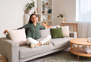 Beautiful happy young woman relaxing on sofa in living room - obrazy, fototapety, plakaty
