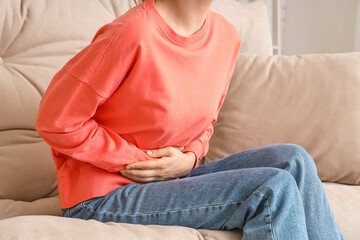Fototapeta premium Young woman suffering from stomach ache on sofa at home, closeup