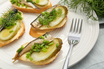 Delicious sandwiches with sprats, pickled cucumber, green onion and dill on plate, closeup