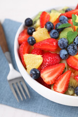 Delicious fresh fruit salad in bowl served on white table, closeup