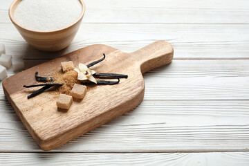 Board with aromatic vanilla sugar, flower and sticks on white wooden background
