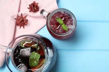 Delicious iced hibiscus tea with mint and dry flowers on light blue wooden table, flat lay. Space for text
