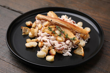Plate with baked salsify roots, lemon and rice on wooden table, closeup
