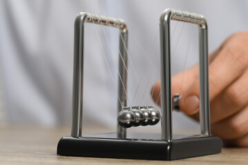 Man playing with Newton's cradle at table, closeup. Physics law of energy conservation