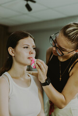 A young makeup artist applies foundation to a girl s face.