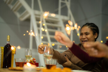 happy female and friends holding sparkler fireworks in a party with Christmas tree. young Asian people enjoy celebrating Christmas and New Year. celebrate with food wine and friendship for love,
