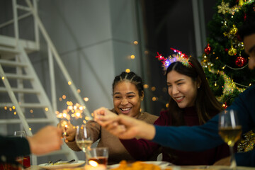 happy female and friends holding sparkler fireworks in a party with Christmas tree. young Asian people enjoy celebrating Christmas and New Year. celebrate with food wine and friendship for love,
