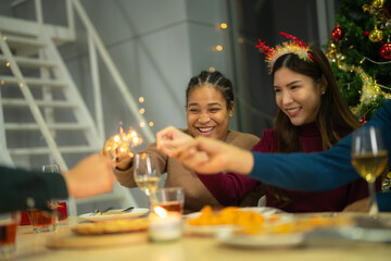 happy female and friends holding sparkler fireworks in a party with Christmas tree. young Asian people enjoy celebrating Christmas and New Year. celebrate with food wine and friendship for love,