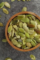 Wooden bowl with peeled pumpkin seeds on grey table, flat lay