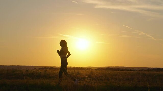 Run for your sunny dream. Training jogging. Healthy beautiful girl is engaged in fitness, jogging in country in sun. Jogger girl breathes in outdoors. Free young woman runs in summer park at sunset