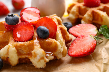 Delicious Belgian waffle with fresh berries and honey on parchment paper, closeup