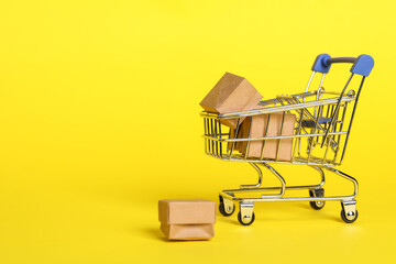 Small metal shopping cart with boxes on yellow background. Space for text
