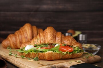 Tasty croissant with salmon, avocado, mozzarella and lettuce on wooden table, closeup