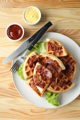 Tasty Belgian waffles served with bacon, lettuce and sauces on wooden table, flat lay