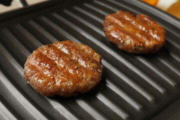 Delicious hamburger patties on electric grill, closeup