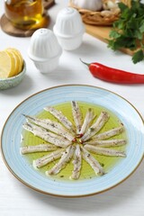 Tasty pickled anchovies with spices and products on white wooden table