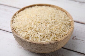 Raw rice in bowl on light wooden table, closeup